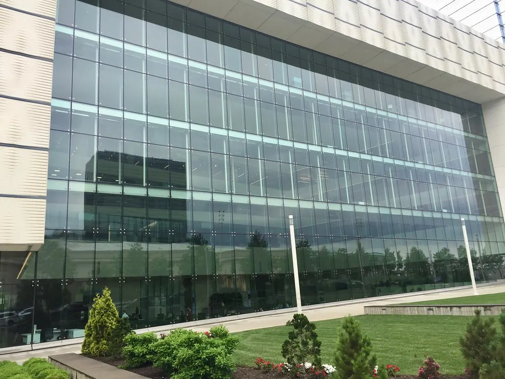 A modern hospital building with a fully glazed frontage over three storeys, seen across a lawn and a low hedge.